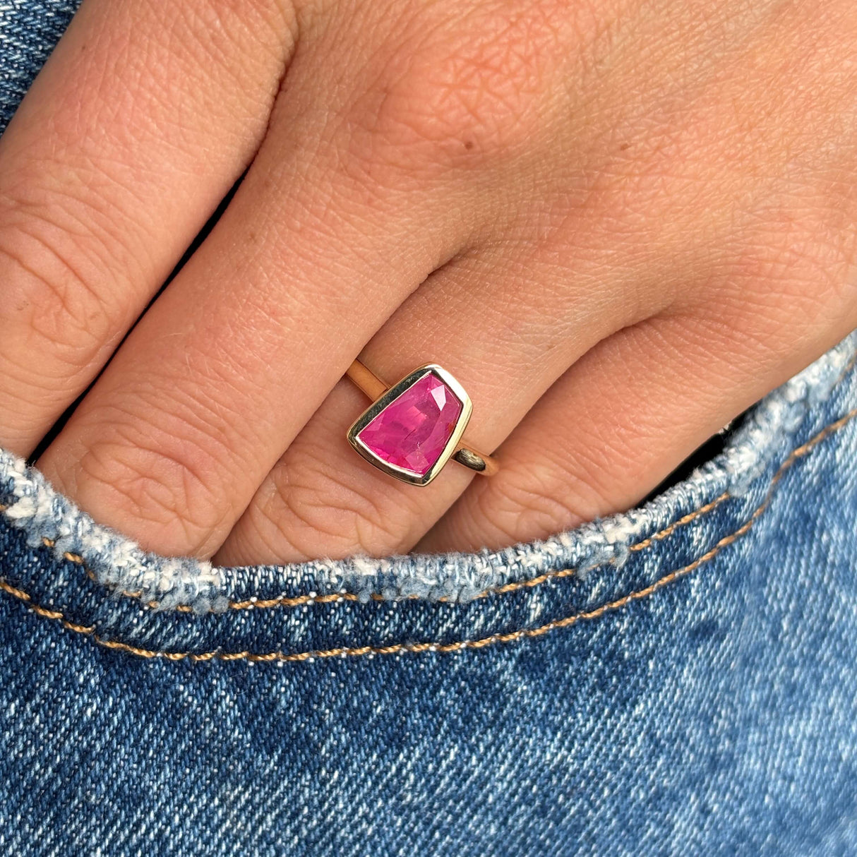 Hand wearing a gold Vintage-inspired, pink ruby solitaire engagement ring against a denim background