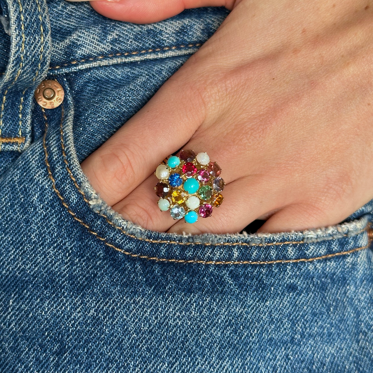 Multi gemstone cluster ring worn on hand in pocket of jeans, front view.