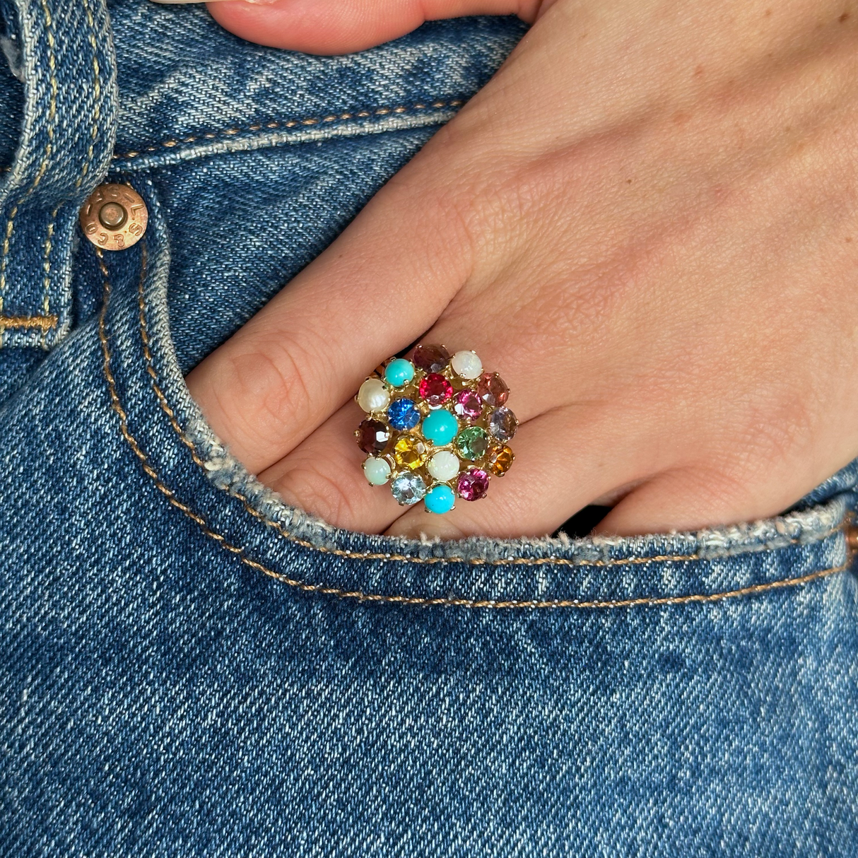  Multi gemstone cluster ring worn on hand in pocket of jeans, front view.