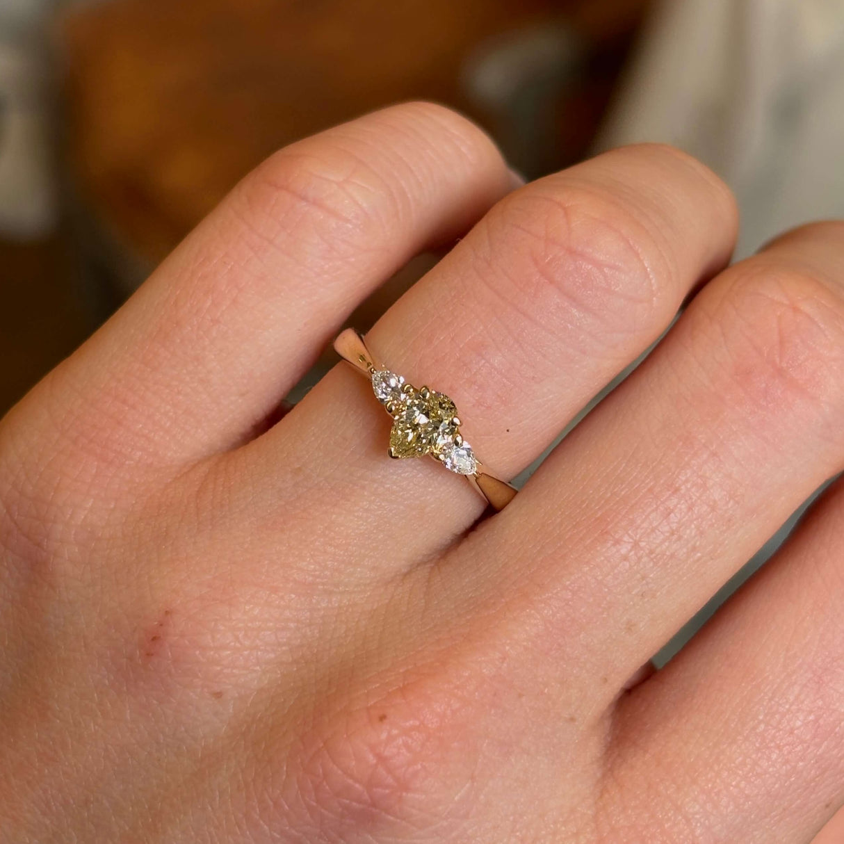 Pear-cut diamond three-stone engagement ring worn on hand shown close up.