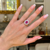 Pink sapphire and diamond cluster ring worn on hand.