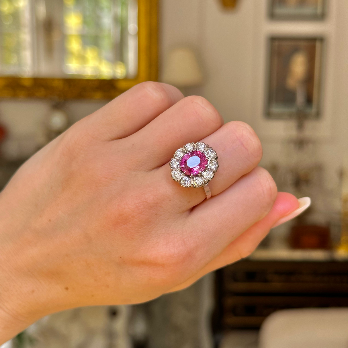 Pink sapphire and diamond cluster ring worn on closed hand.