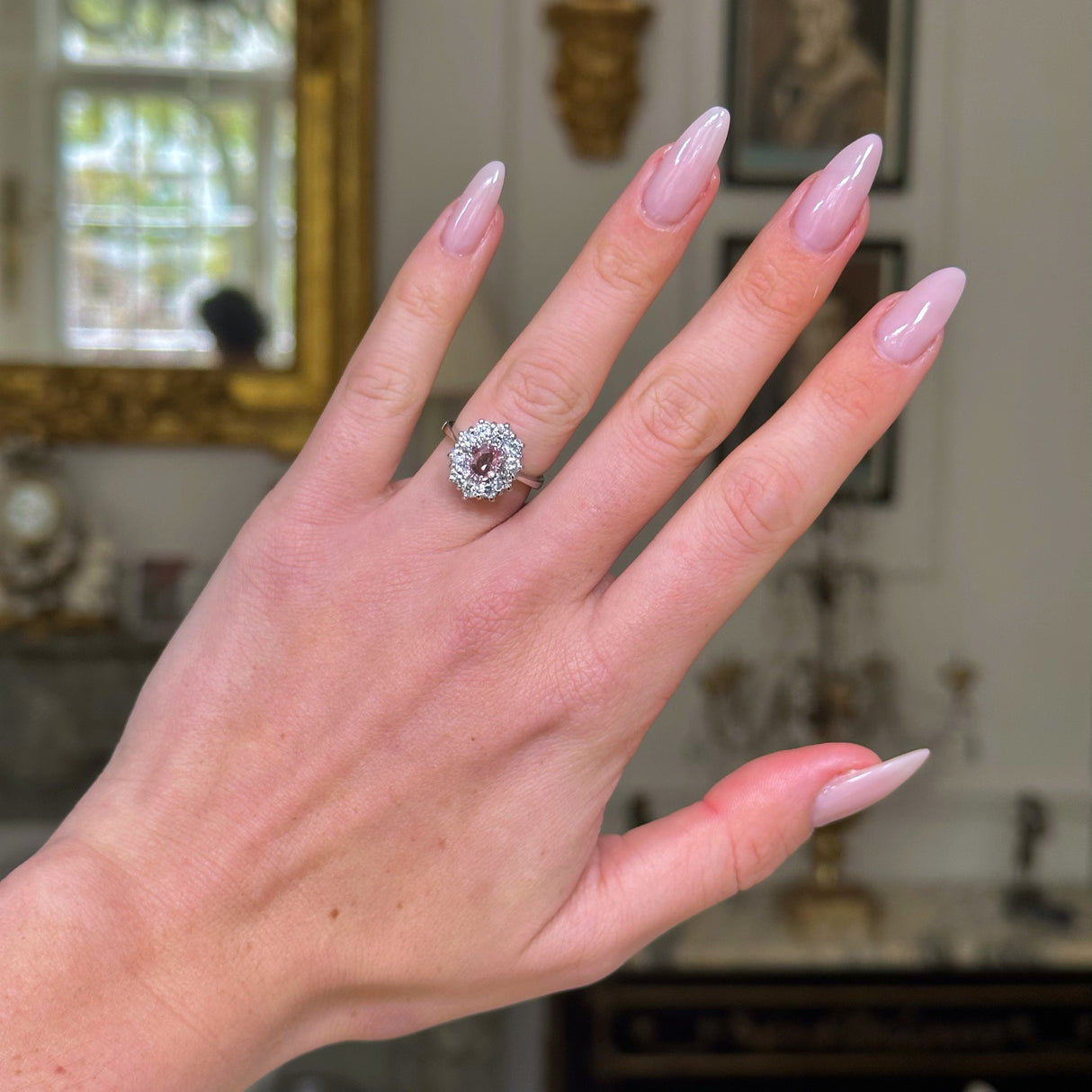 Peach pink sapphire diamond cluster ring worn on hand.