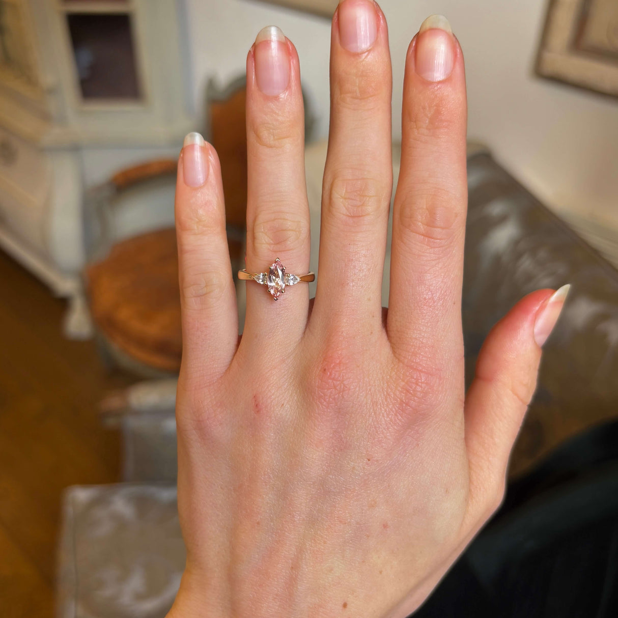 Pink Marquise-cut sapphire and diamond three-stone engagement ring on the hand at a distance showing scale.