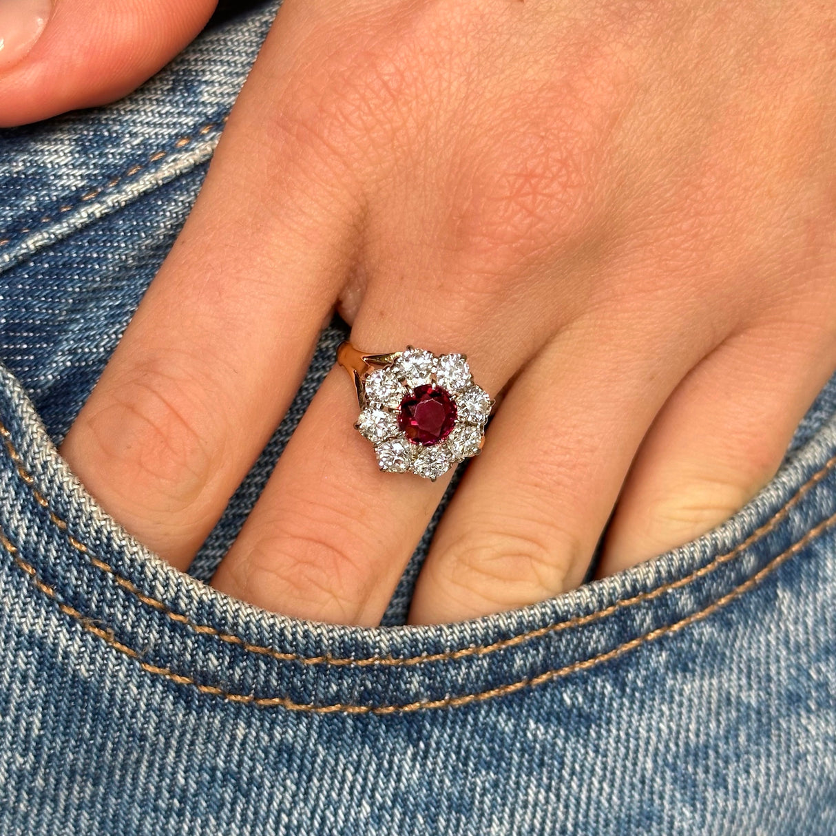 antique ruby and diamond cluster ring worn on the middle finger on a hand placed into the pocket of denim jeans.