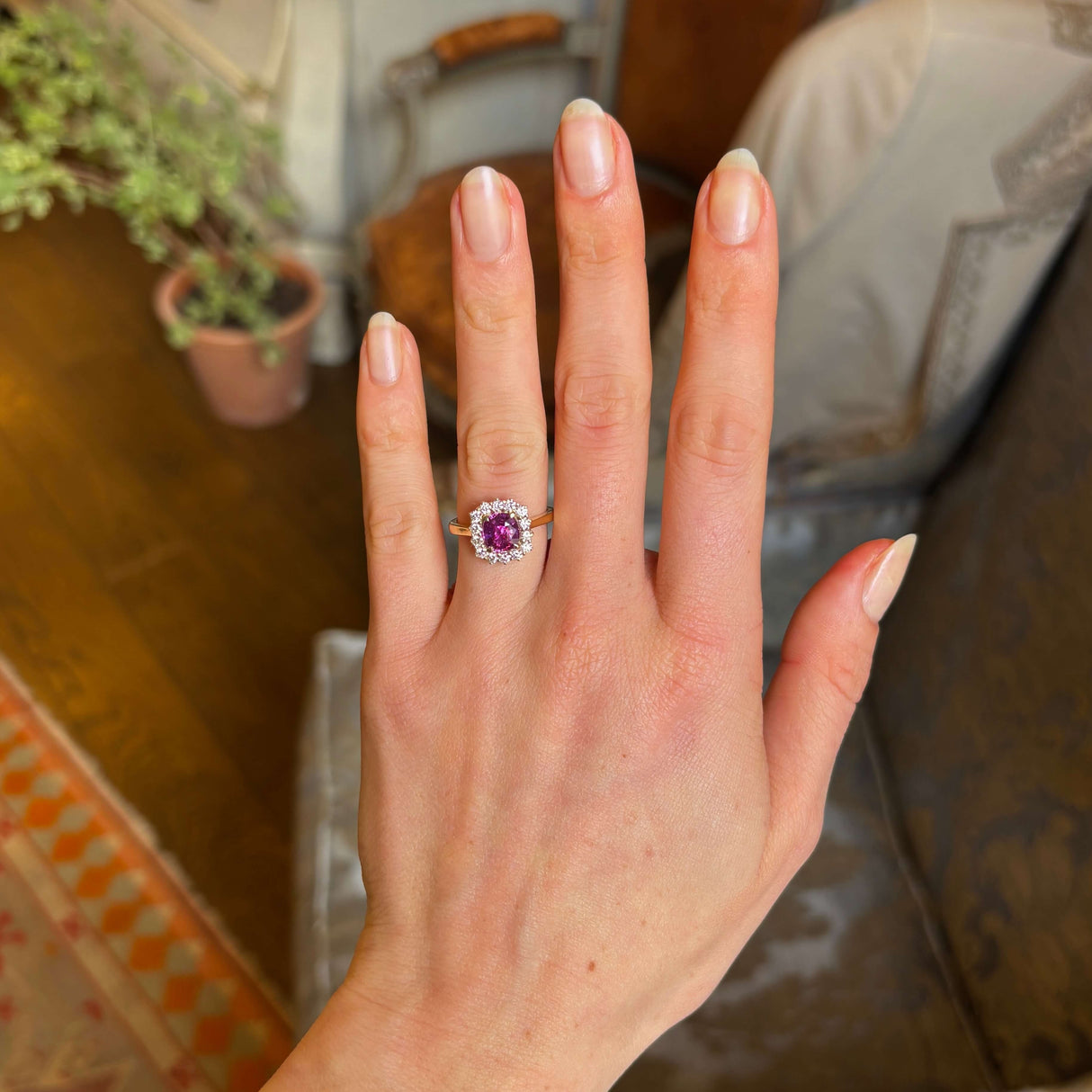 Square-cut pink sapphire and diamond cluster engagement ring worn on the ring finger of the left hand