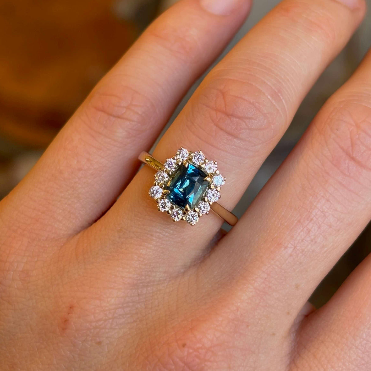 Teal sapphire and diamond clusterengagement ring show up close on ring finger of left hand