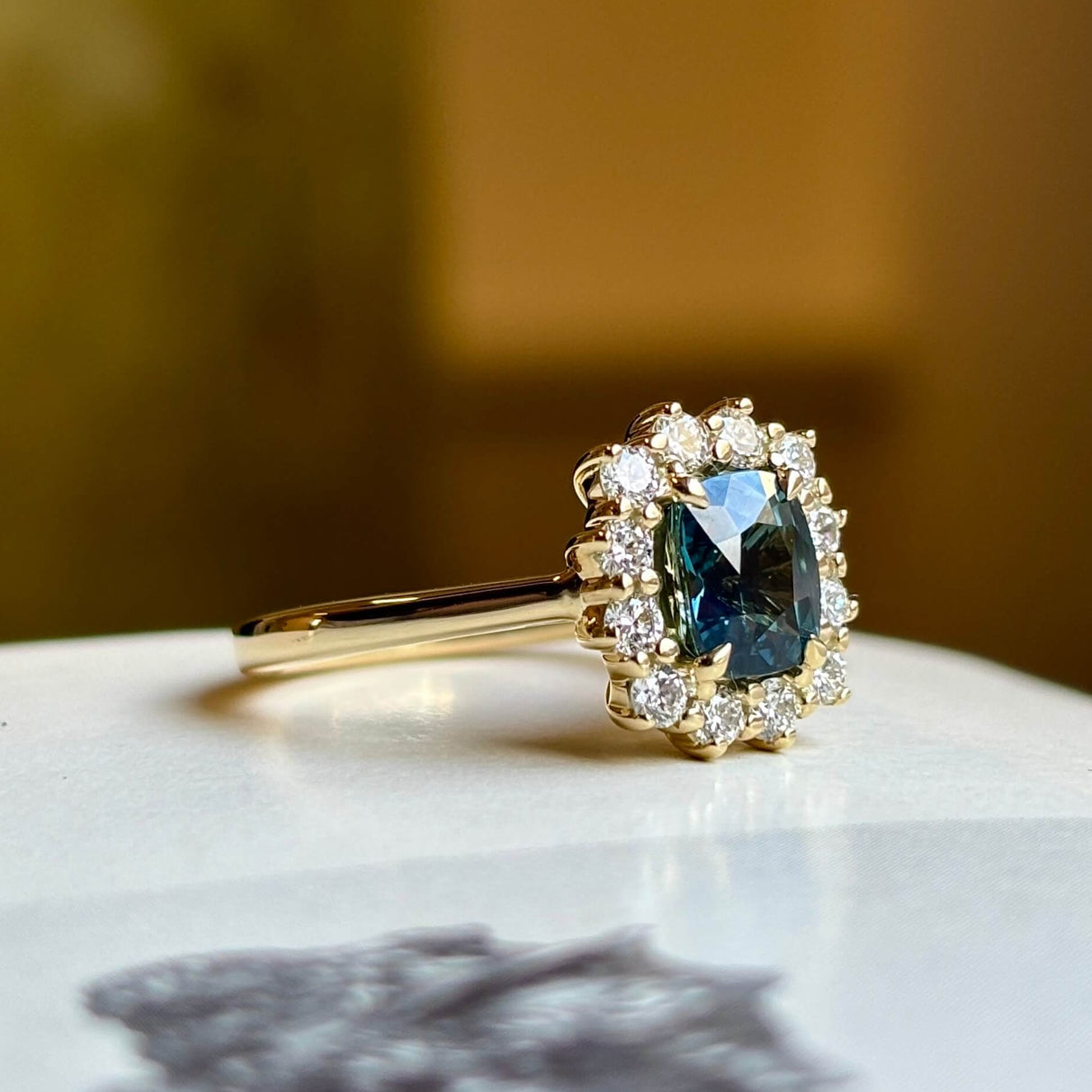 Teal sapphire and diamond cluster ring in yellow gold, positioned to the side in close-up.
