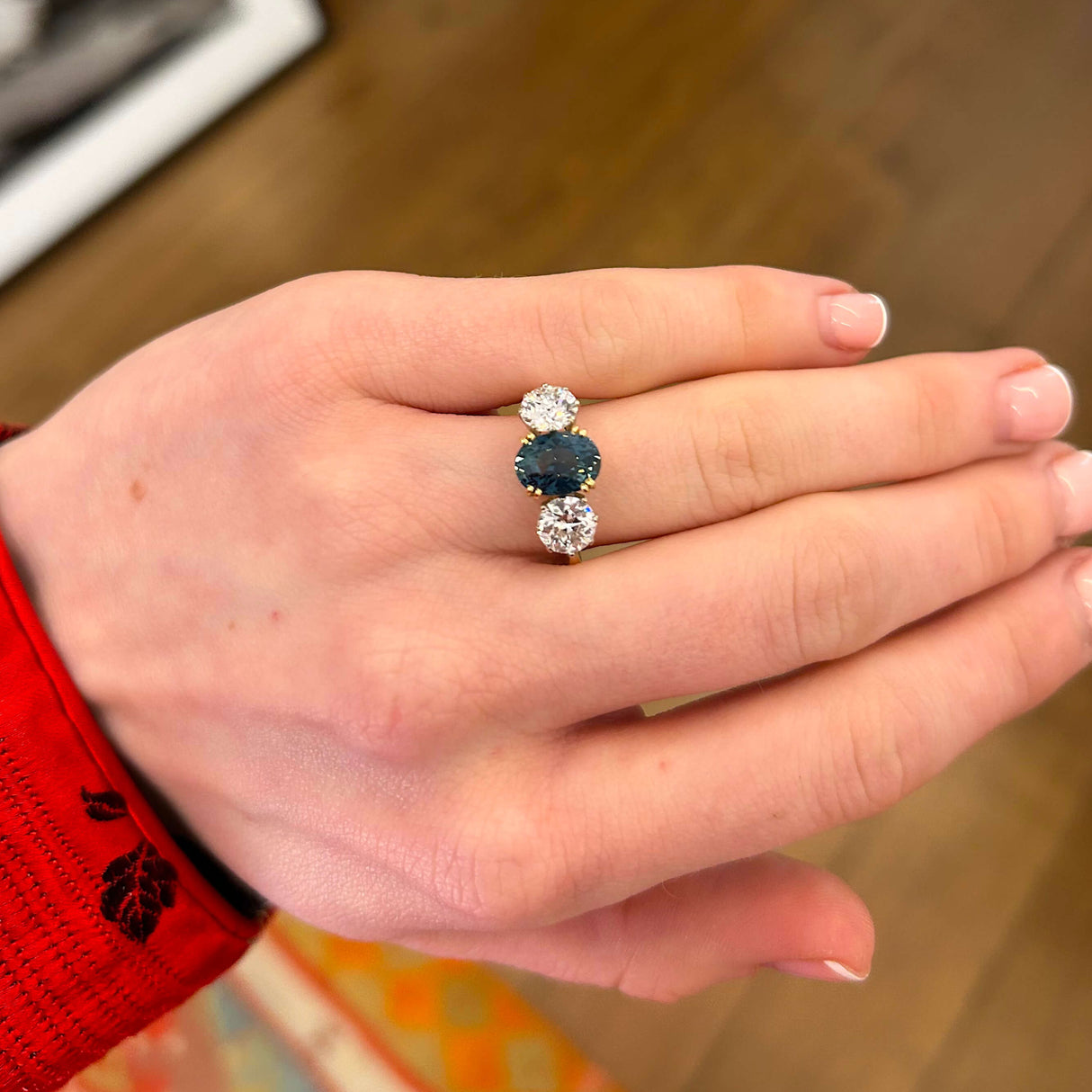 Teal sapphire three-stone ring worn in the hand in lower lighting conditions