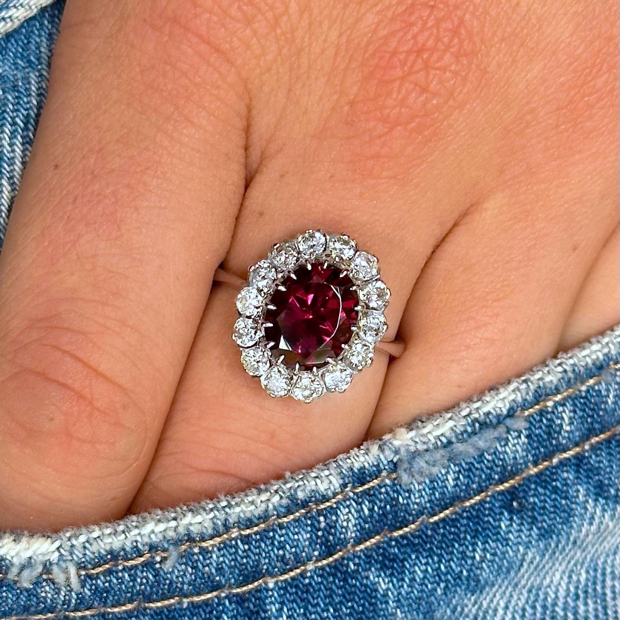 red tourmaline and diamond cluster ring, worn on hand and placed in pocket of jeans, front view.