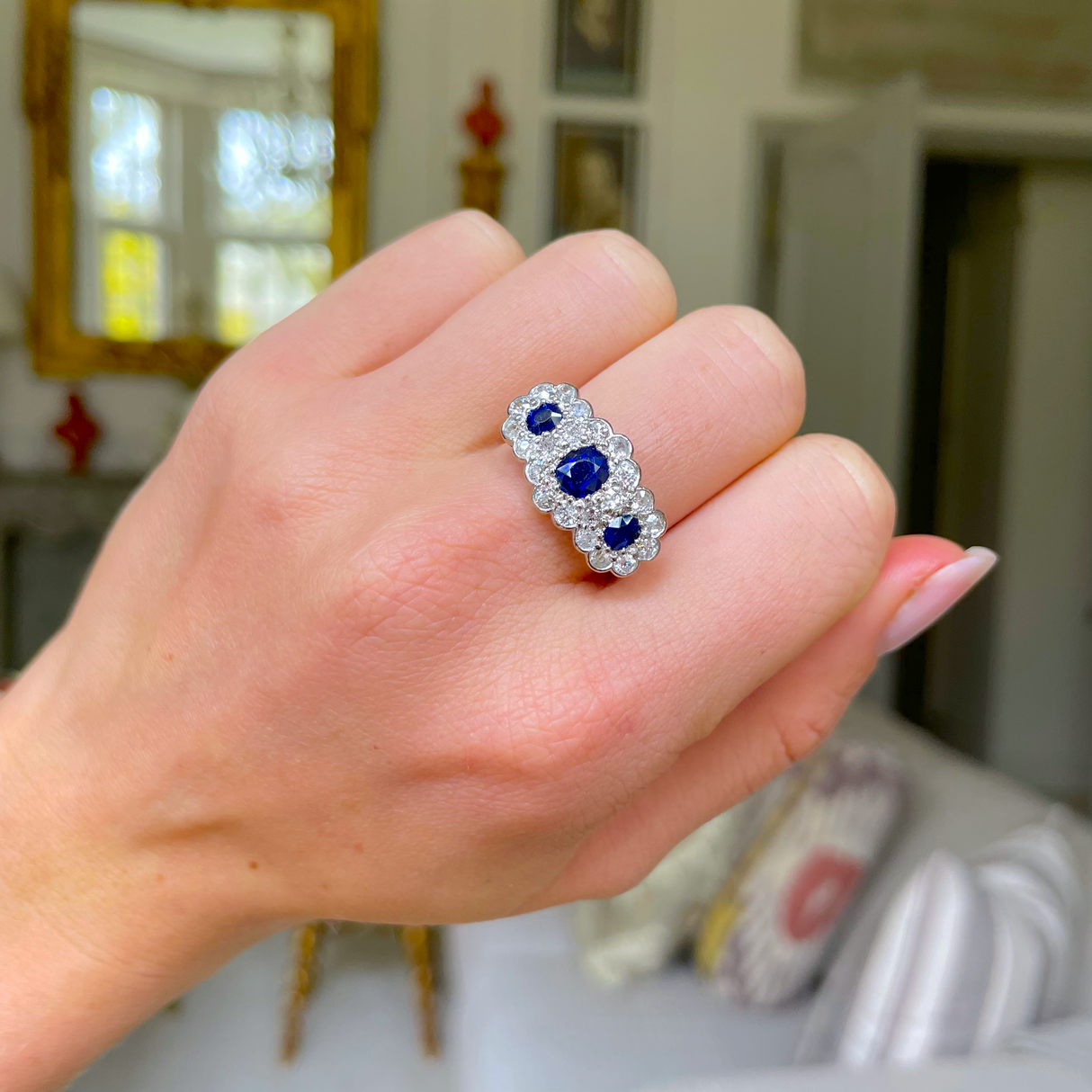 Antique sapphire and diamond triple cluster ring worn on hand.