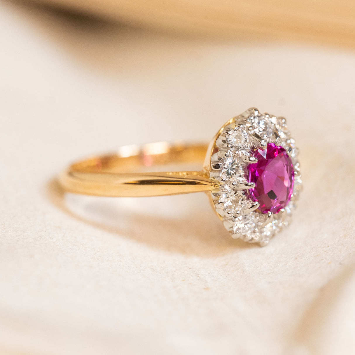 Vintage gold ring with a pink ruby gemstone and diamond halo on a light background.