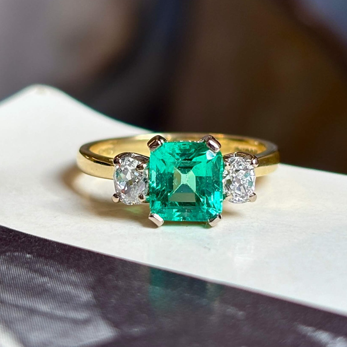 Vintage, emerald and diamond three-stone engagement ring on vintage book with blurred background.