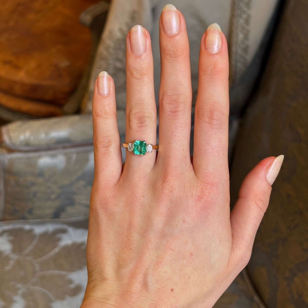 Vintage, emerald and diamond three-stone engagement ring worn on hand.