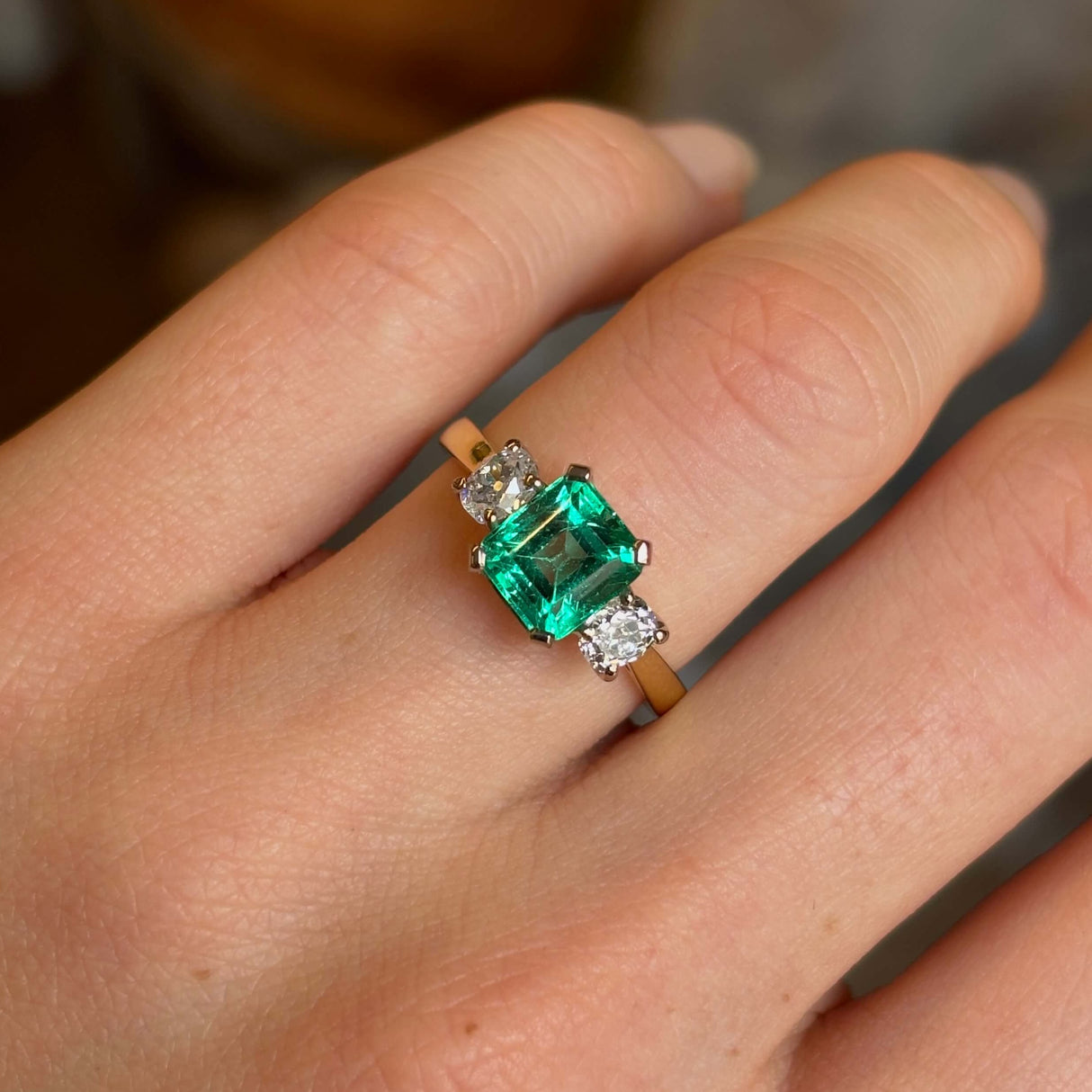 Vintage, emerald and diamond three-stone engagement ring worn on hand close up.