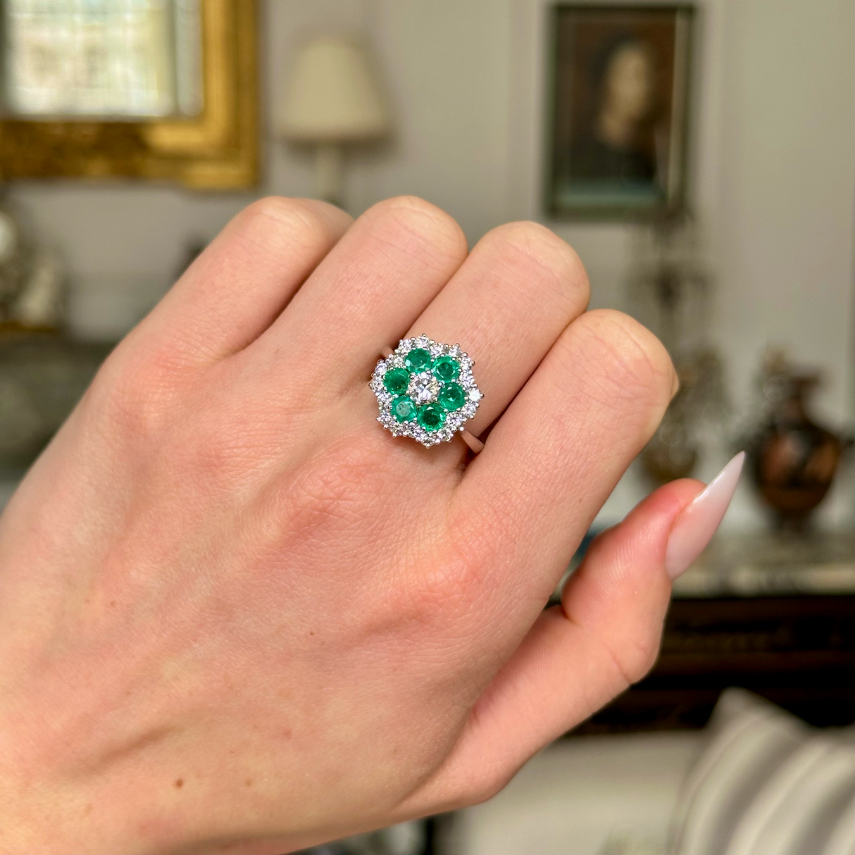 Vintage emerald and diamond cluster ring worn on closed hand, front view.