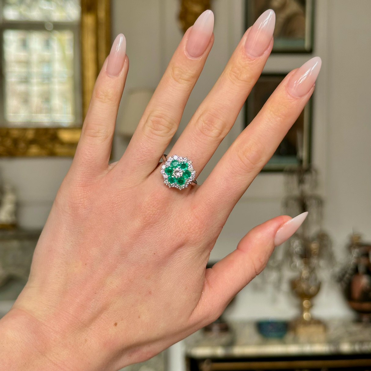 Vintage emerald and diamond cluster ring worn on hand, front view.