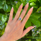 Vintage, cornflower blue sapphire & diamond cluster engagement ring worn on hand. 