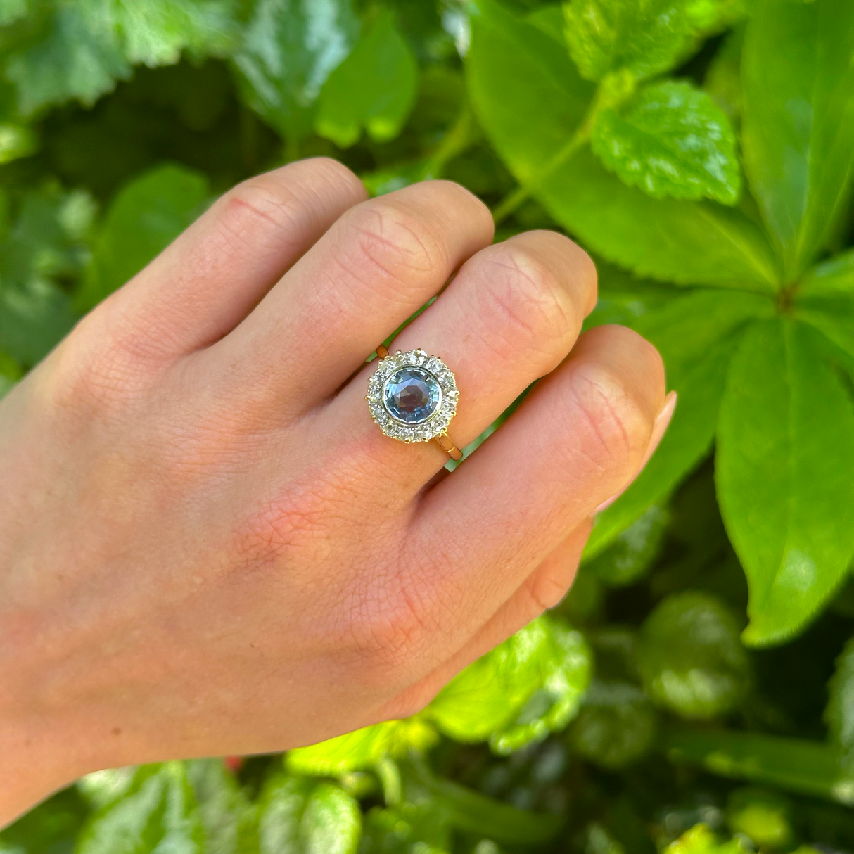 Vintage, cornflower blue sapphire & diamond cluster engagement ring worn on hand. 