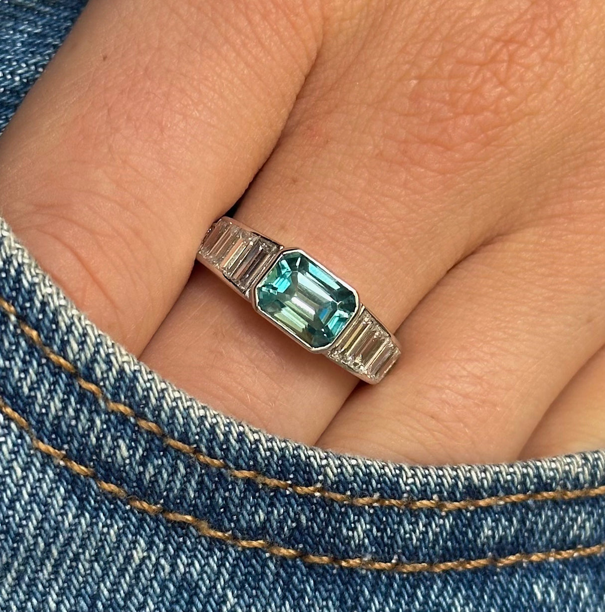 Vintage zircon and diamond ring, worn on hand and placed in pocket of denim jeans, front view.