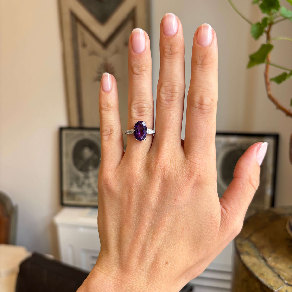 Antique Art Deco platinum ring worn on hand, showcasing a vibrant purple amethyst centre stone accented by brilliant diamonds in an elegant three-stone design.