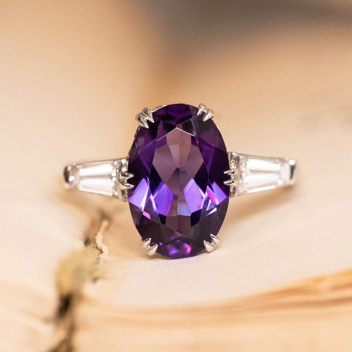 Antique Art Deco amethyst and diamond three-stone ring featuring an oval-cut amethyst flanked by tapered baguette diamonds in platinum.