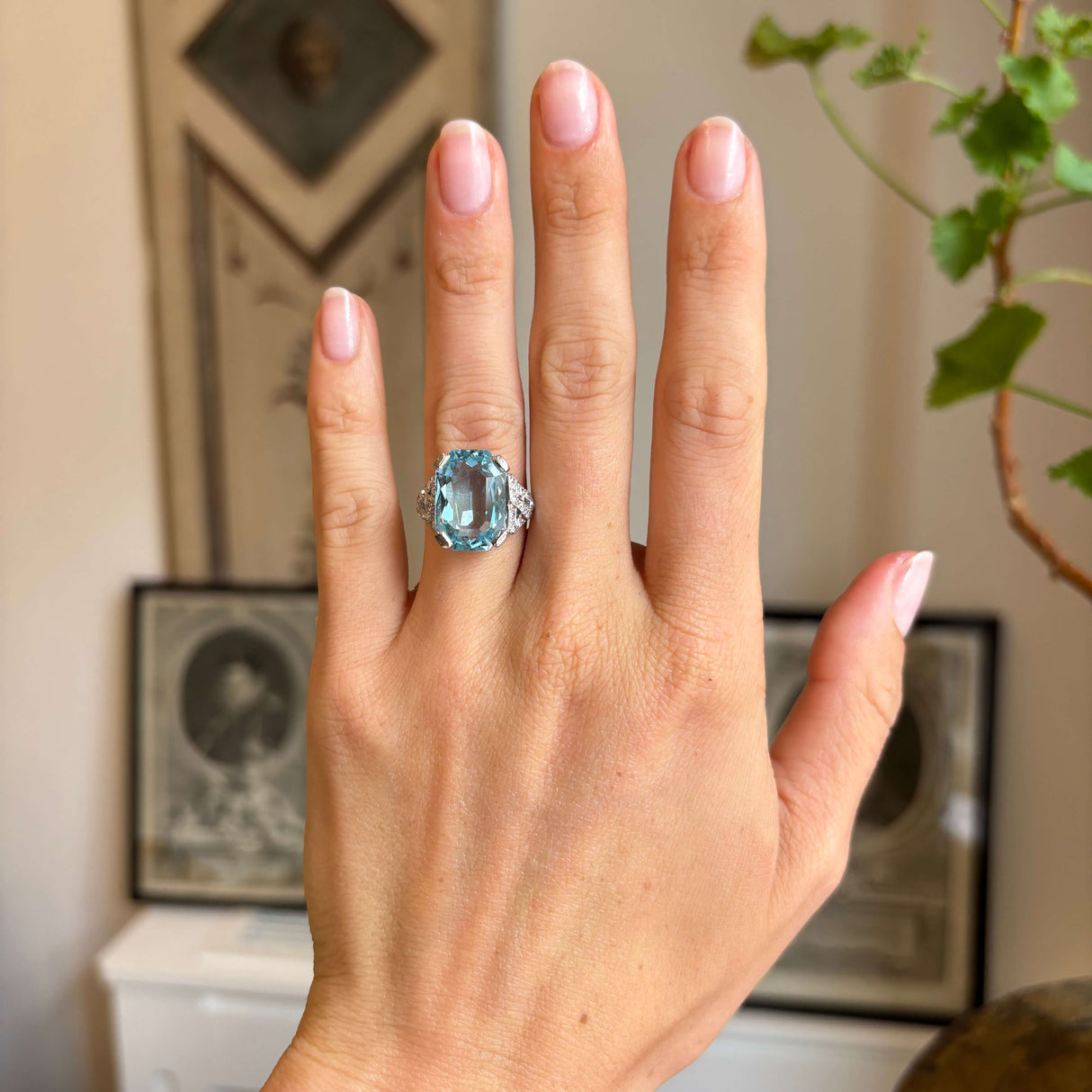 Antique Art Deco aquamarine and diamond cocktail ring in platinum worn on hand, displaying a large blue aquamarine and diamond cluster against a warm vintage-inspired interior setting.