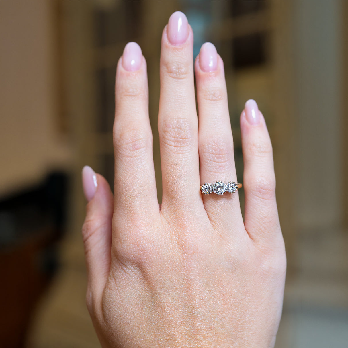 Antique Art Deco diamond three-stone ring worn on hand with yellow gold band.