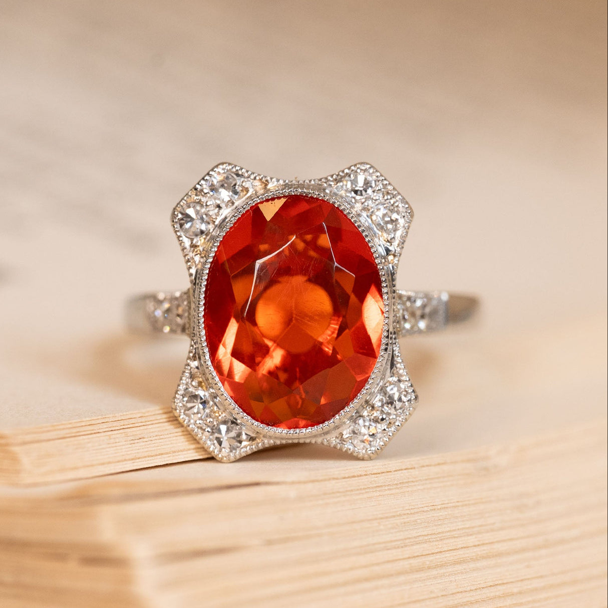 Antique Art Deco fire opal and diamond cluster ring featuring a vivid orange fire opal framed by old-cut diamonds in a geometric platinum setting.