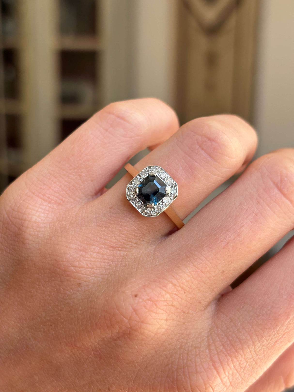 Antique Art Deco sapphire and diamond cluster engagement ring featuring a blue sapphire centre stone and geometric diamond cluster design, worn on a hand.