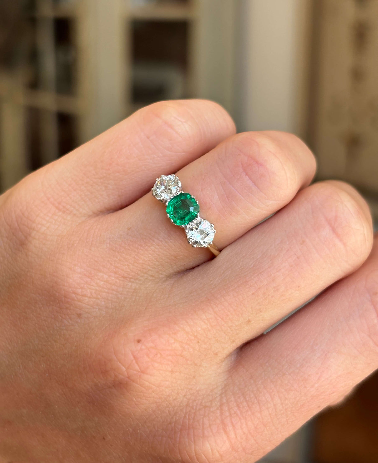 Antique Edwardian emerald and diamond three-stone engagement ring featuring a vibrant emerald centre stone and diamond accents, worn on a hand.