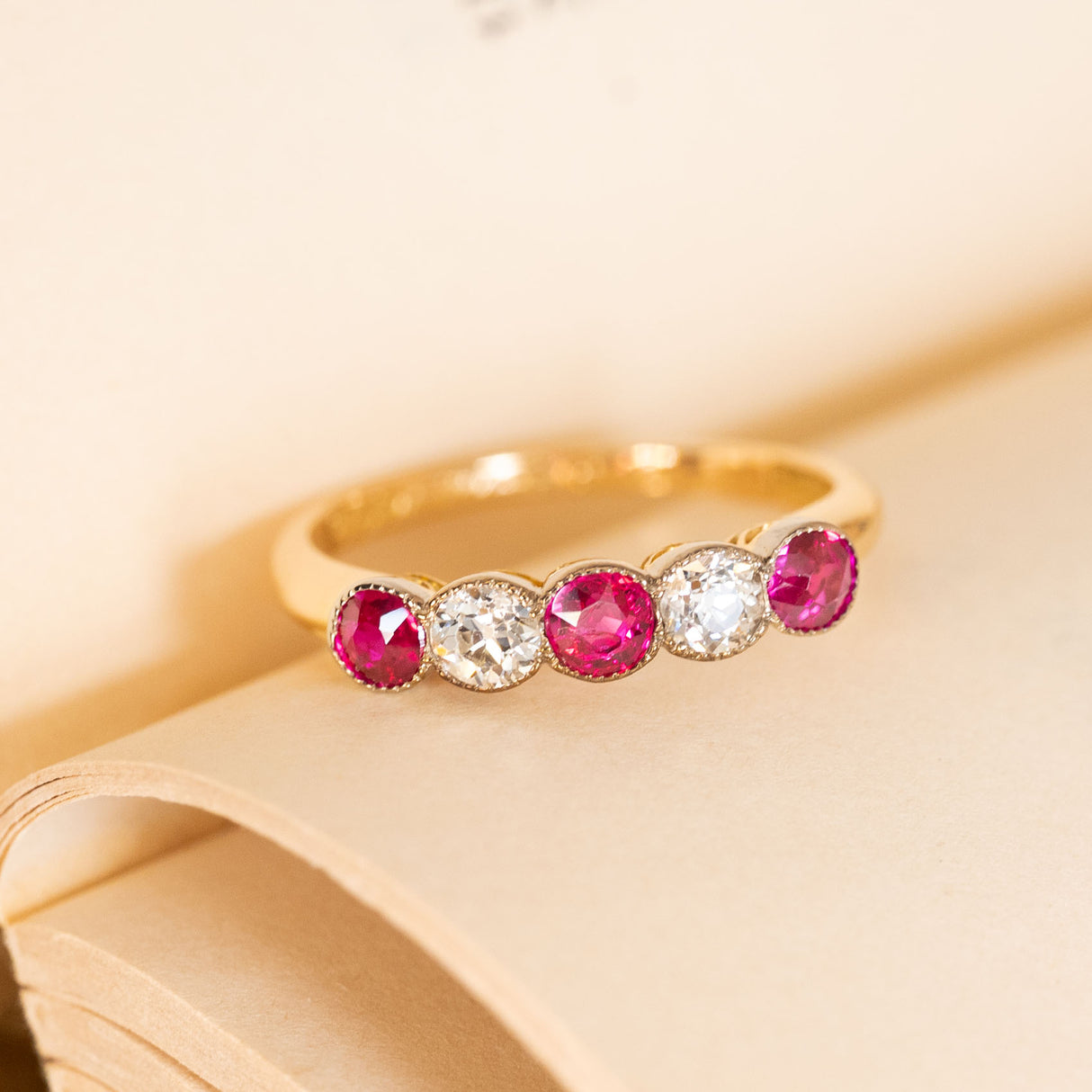Antique five-stone ring set with rich pinkish-red rubies and old-cut diamonds, creating a timeless Edwardian design in yellow gold.
