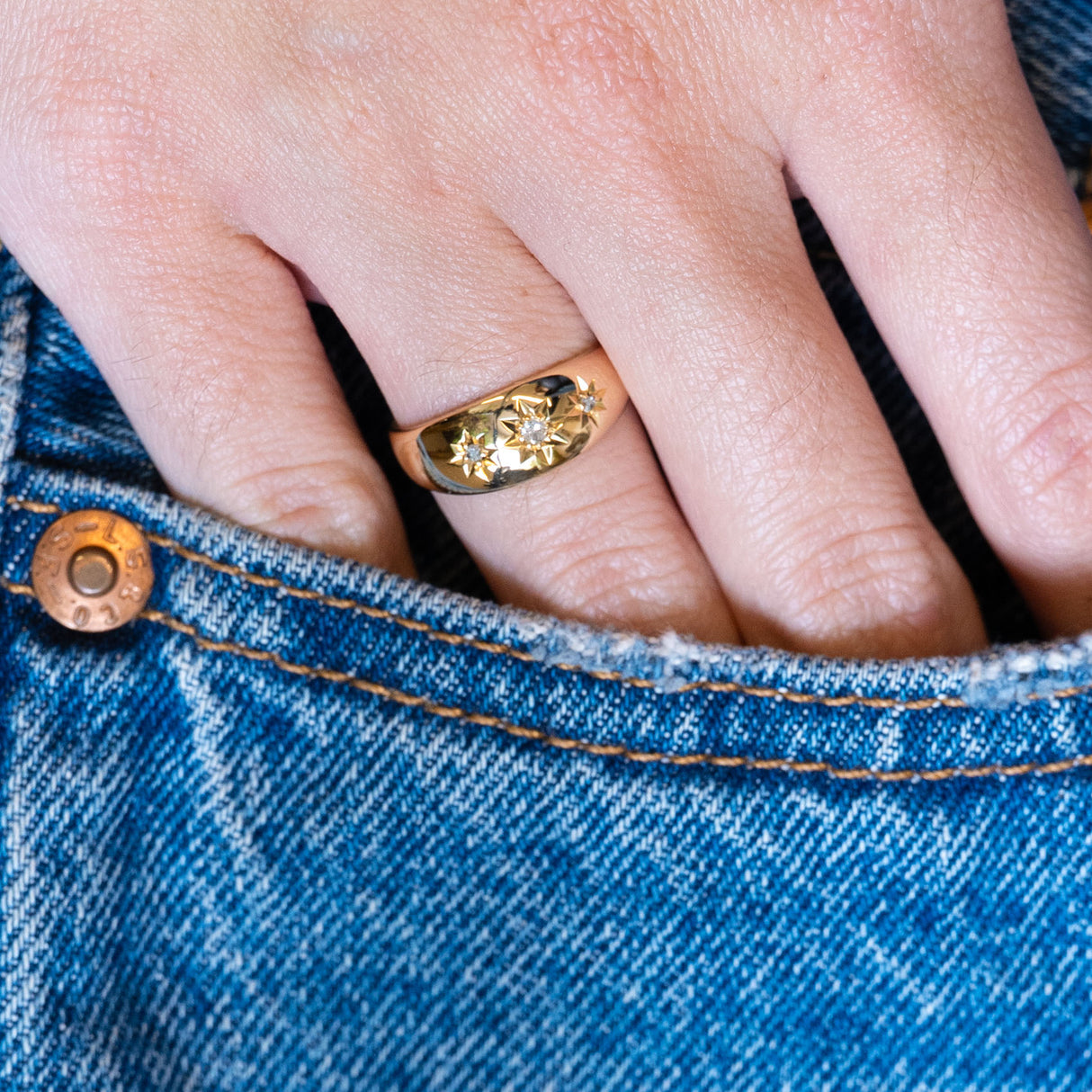 Antique Edwardian three-stone diamond gypsy ring worn with hand resting in denim pocket.