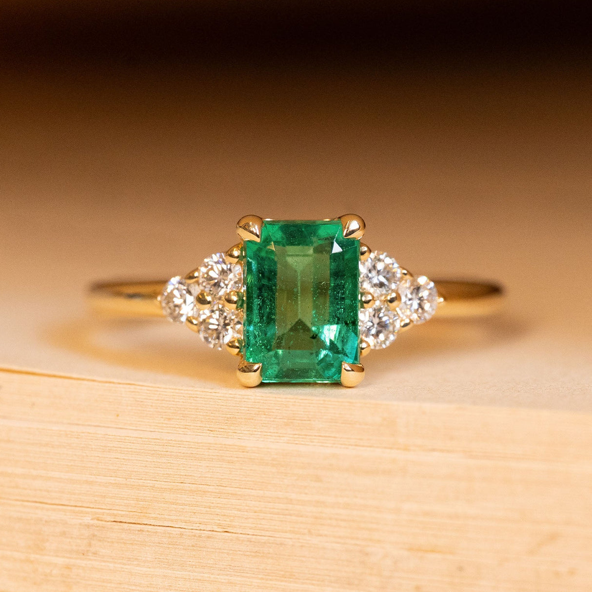 Antique inspired emerald and diamond cluster trefoil engagement ring featuring an emerald-cut emerald with trefoil diamond clusters on each shoulder in yellow gold.