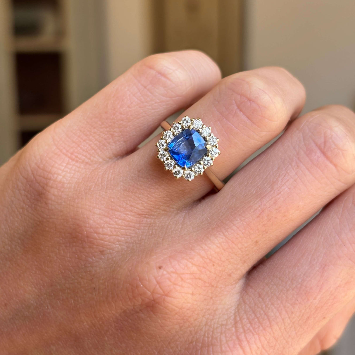 Close-up of an antique-inspired violet-blue cushion cut Sri Lankan sapphire and diamond cluster engagement ring in yellow gold, showcasing the vivid sapphire, sparkling diamond halo and refined craftsmanship.