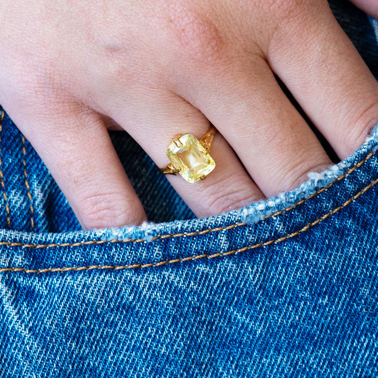 Antique Victorian yellow sapphire solitaire ring worn with hand resting in denim pocket.