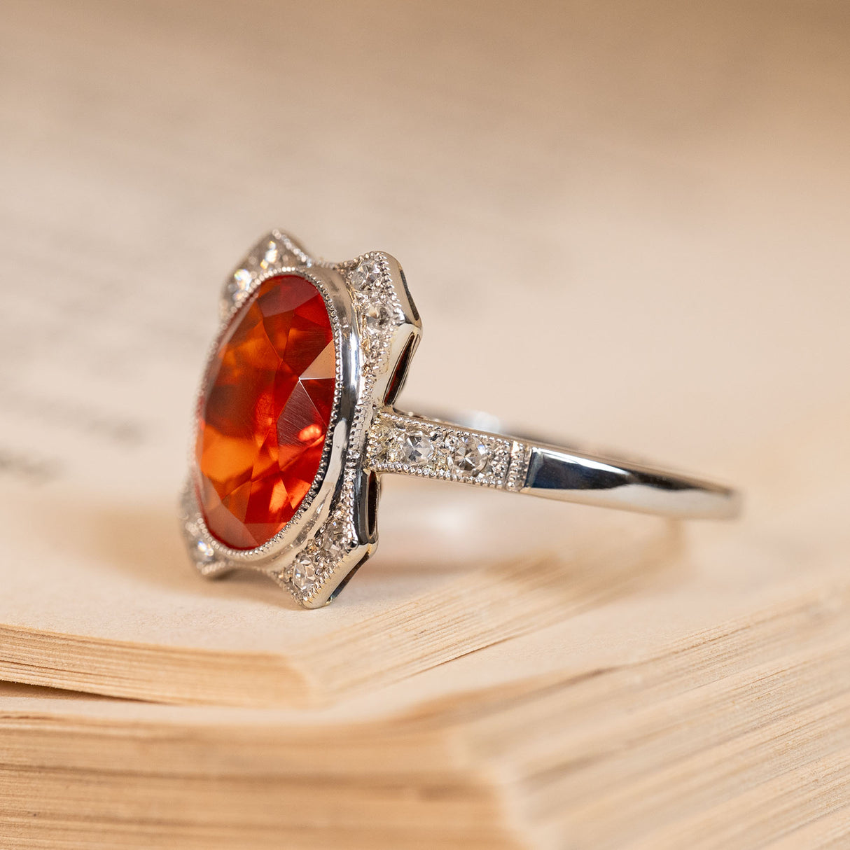 Antique Art Deco fire opal and diamond halo ring with a vibrant oval fire opal surrounded by old-cut diamonds and delicate detailing.