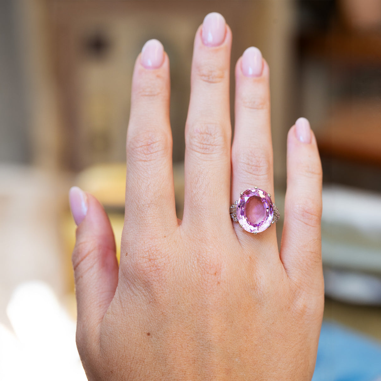 Hand wearing an Art Deco pink topaz and diamond cocktail ring with a blurred background.