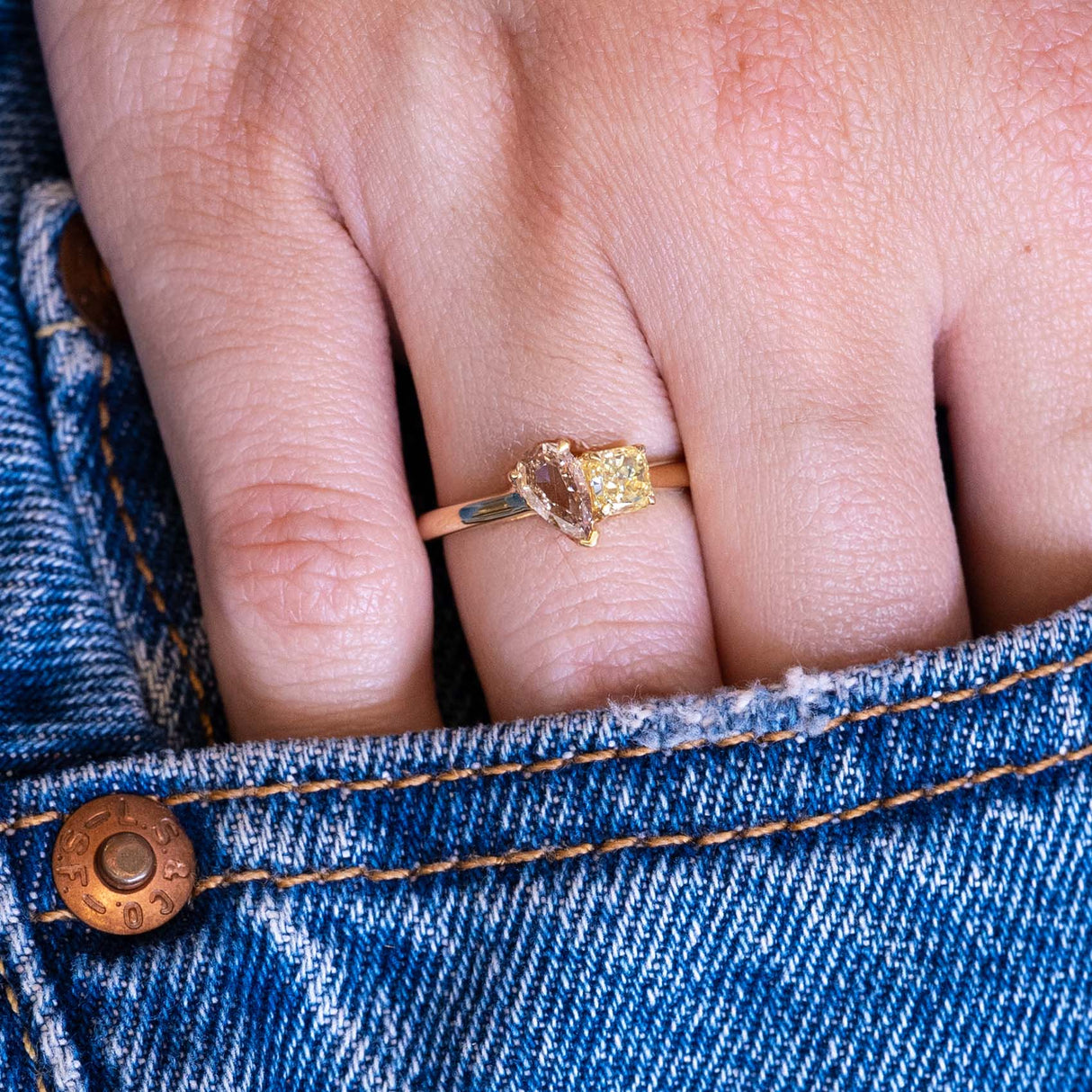Brown and yellow diamond Toi et Moi engagement ring worn on hand with denim pocket styling.