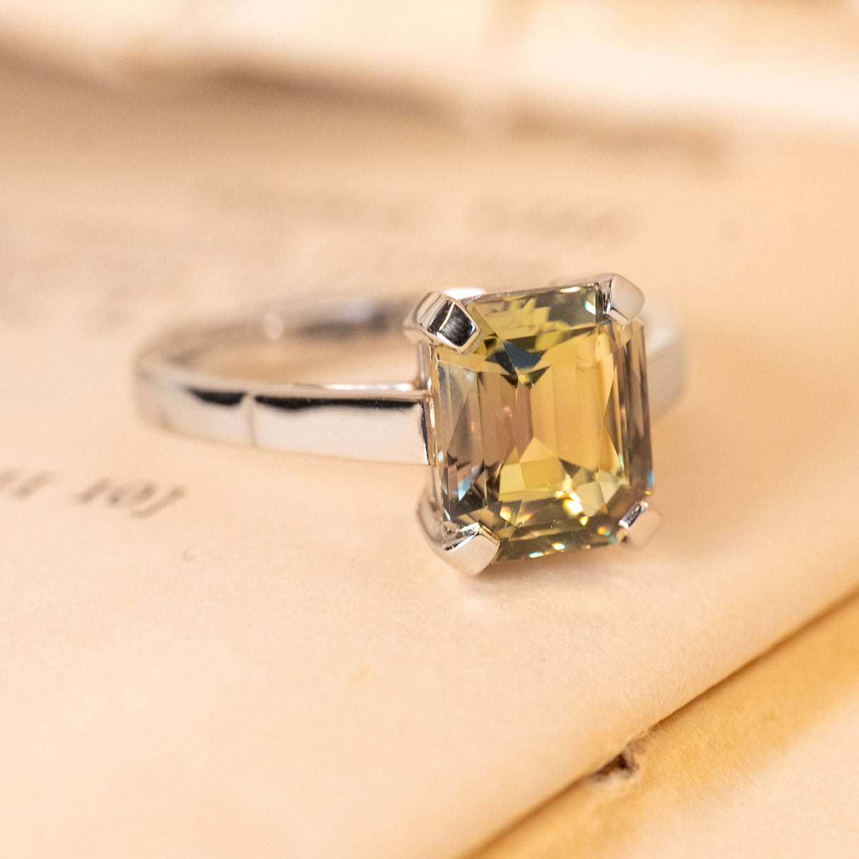 Emerald-cut colour-change sapphire solitaire ring displaying green and brown hues in a classic white gold engagement ring setting.