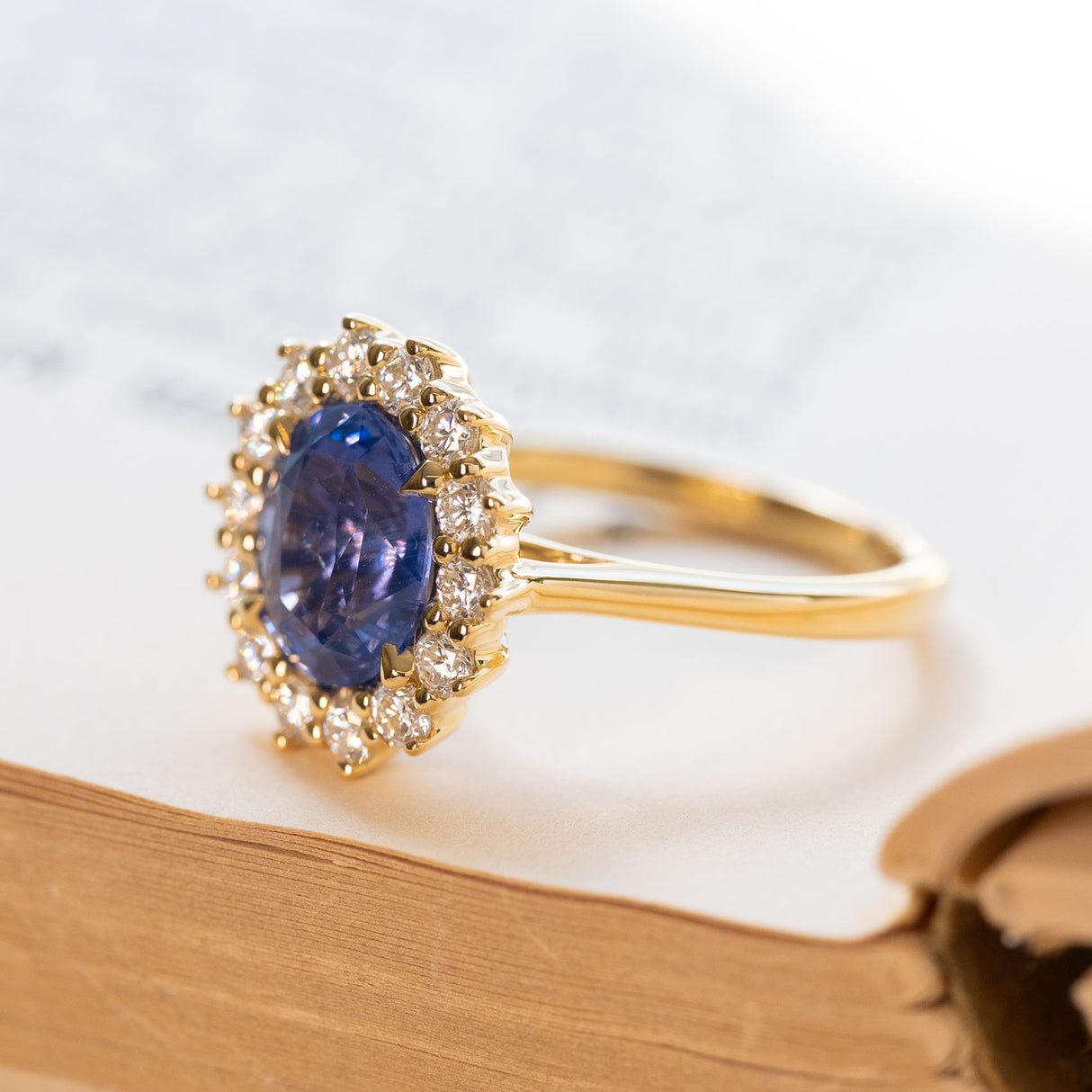 Cornflower blue sapphire and diamond cluster engagement ring with oval sapphire and brilliant-cut diamond halo.