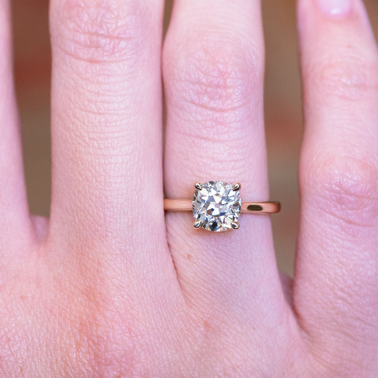 Cushion old-mine cut diamond solitaire engagement ring with claw-set diamond worn on finger.
