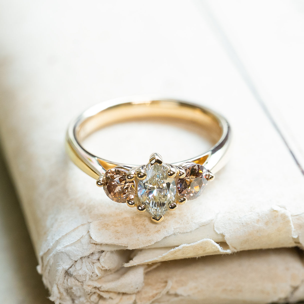 Diamond three-stone engagement ring with marquise-cut centre diamond resting on antique books.