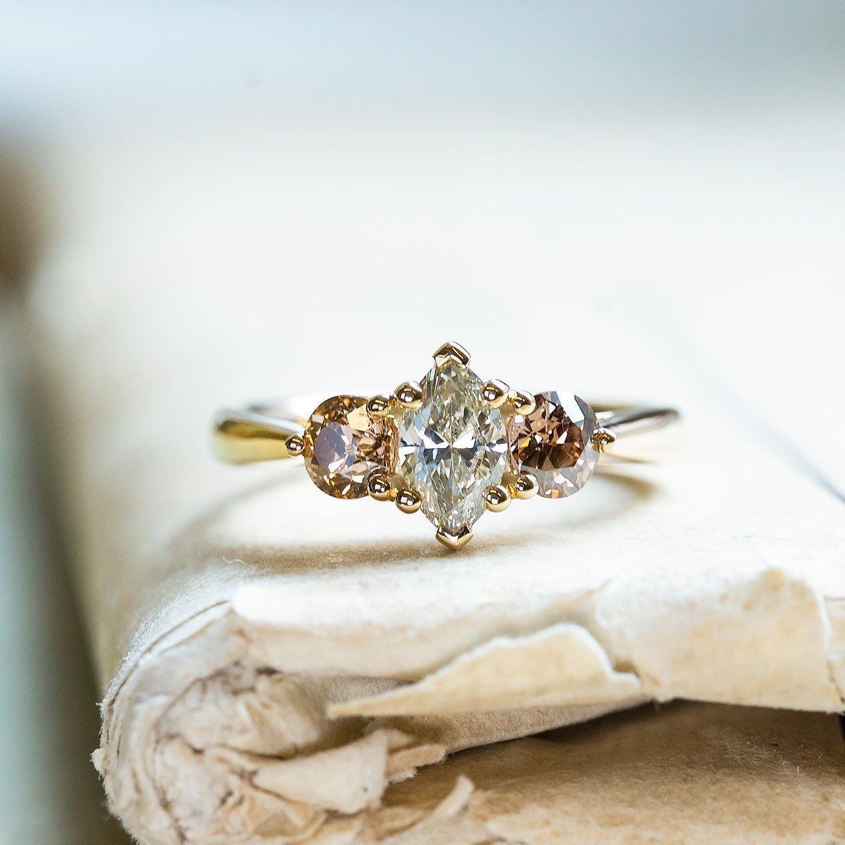 Diamond three-stone engagement ring with marquise-cut centre diamond and diamond side stones on gold band.