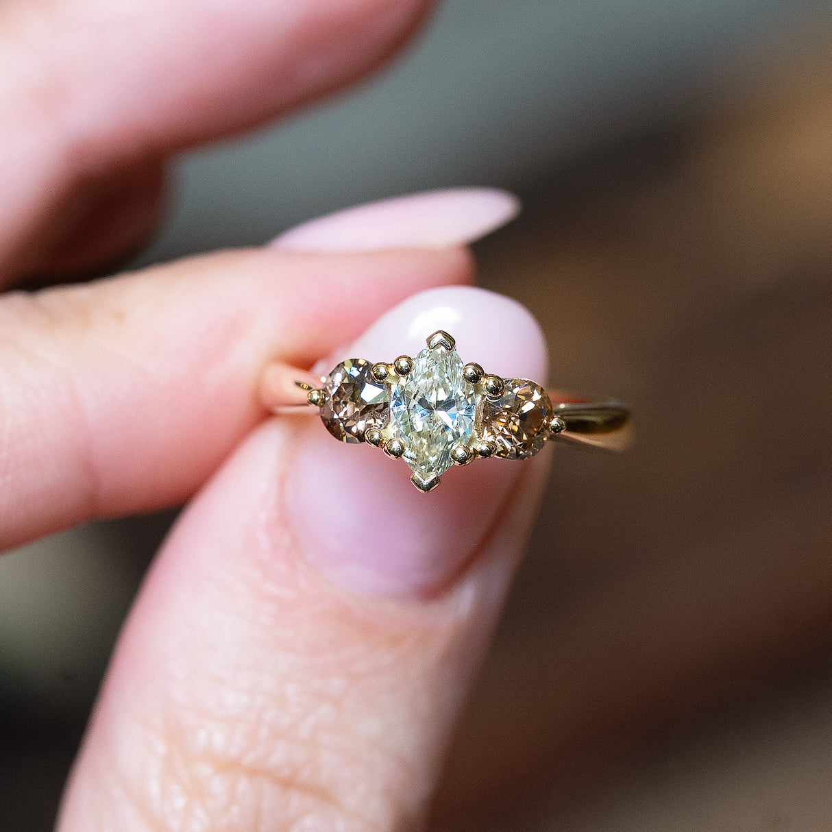 Diamond three-stone engagement ring held between fingers with marquise-cut centre diamond and side stones.
