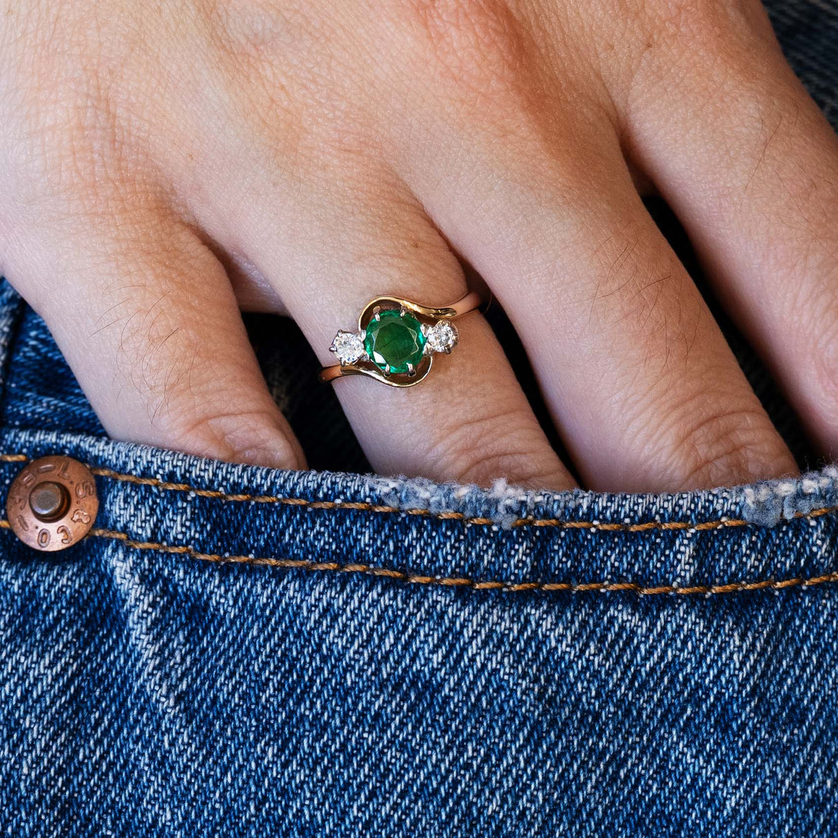 Close-up of a hand wearing an emerald ring on blue denim fabric.