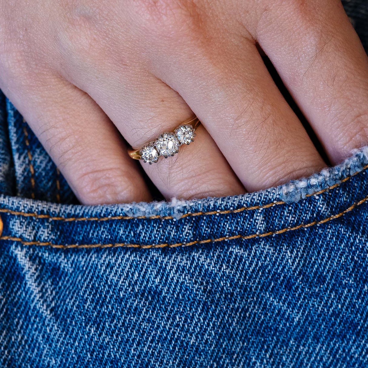 Edwardian diamond three stone ring worn on hand with denim pocket detail.