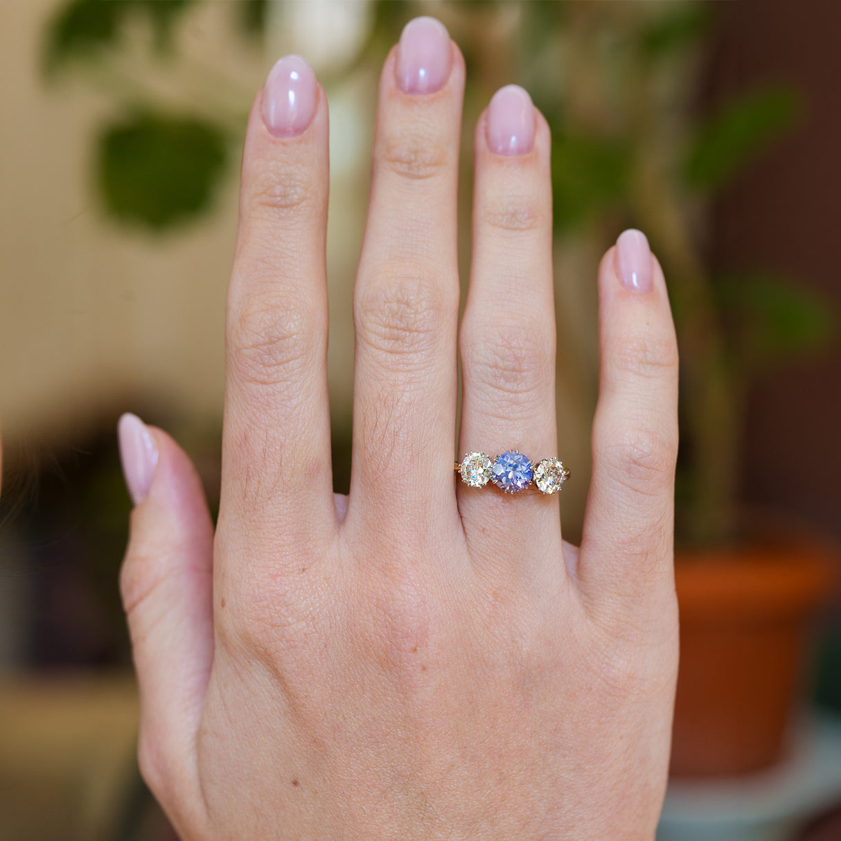 Tthree stone sapphire and diamond ring worn on hand.