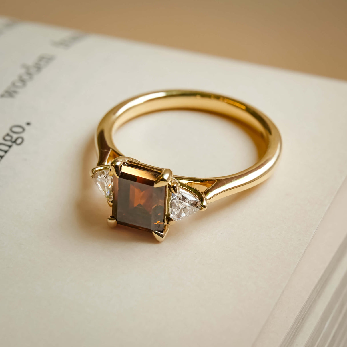 emerald cut brown diamond three stone ring with tapered diamond side stones in yellow gold