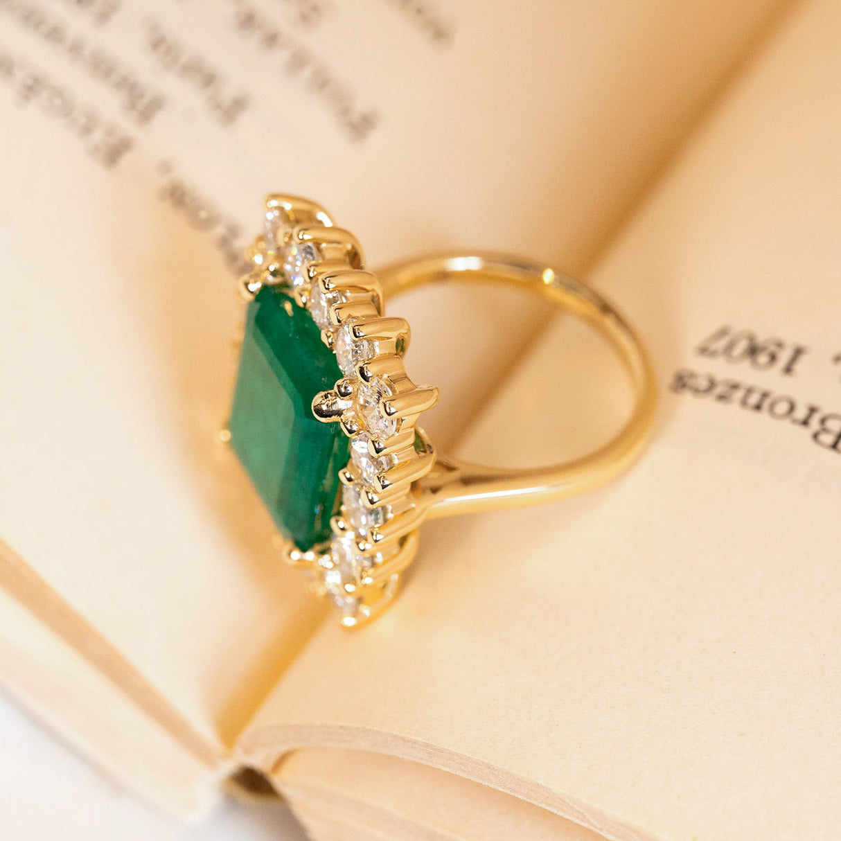 Emerald and diamond cluster cocktail ring with a substantial emerald-cut emerald and dazzling diamond surround set in yellow gold.
